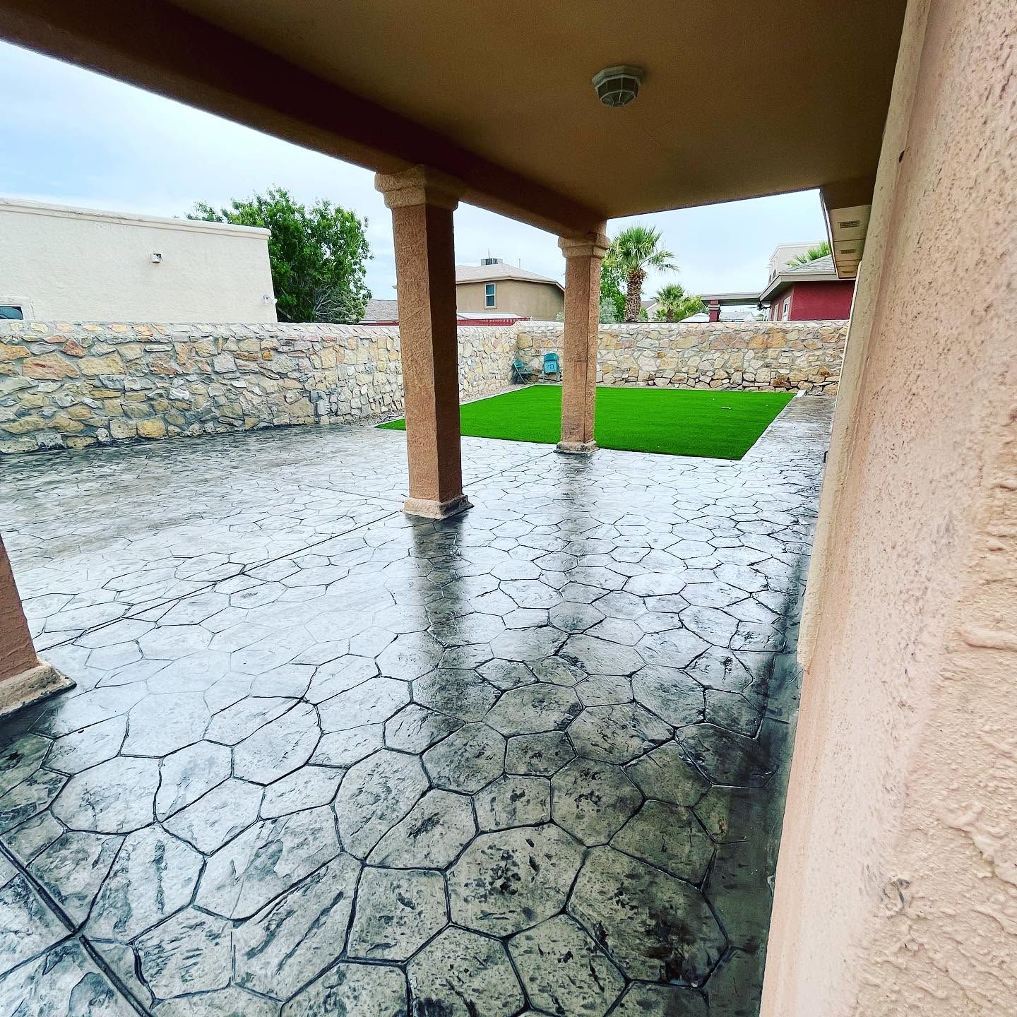Covered patio with stamped concrete floor, stone wall, and a small grassy yard beyond.