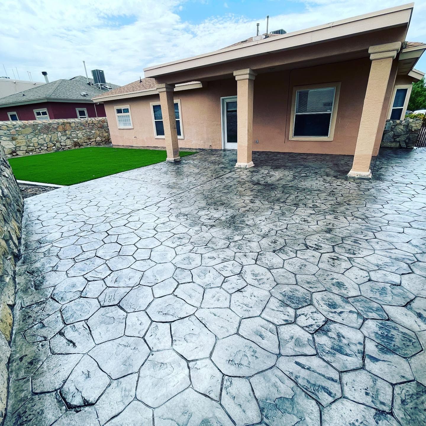 Front yard with stamped concrete patio and covered porch on a tan house