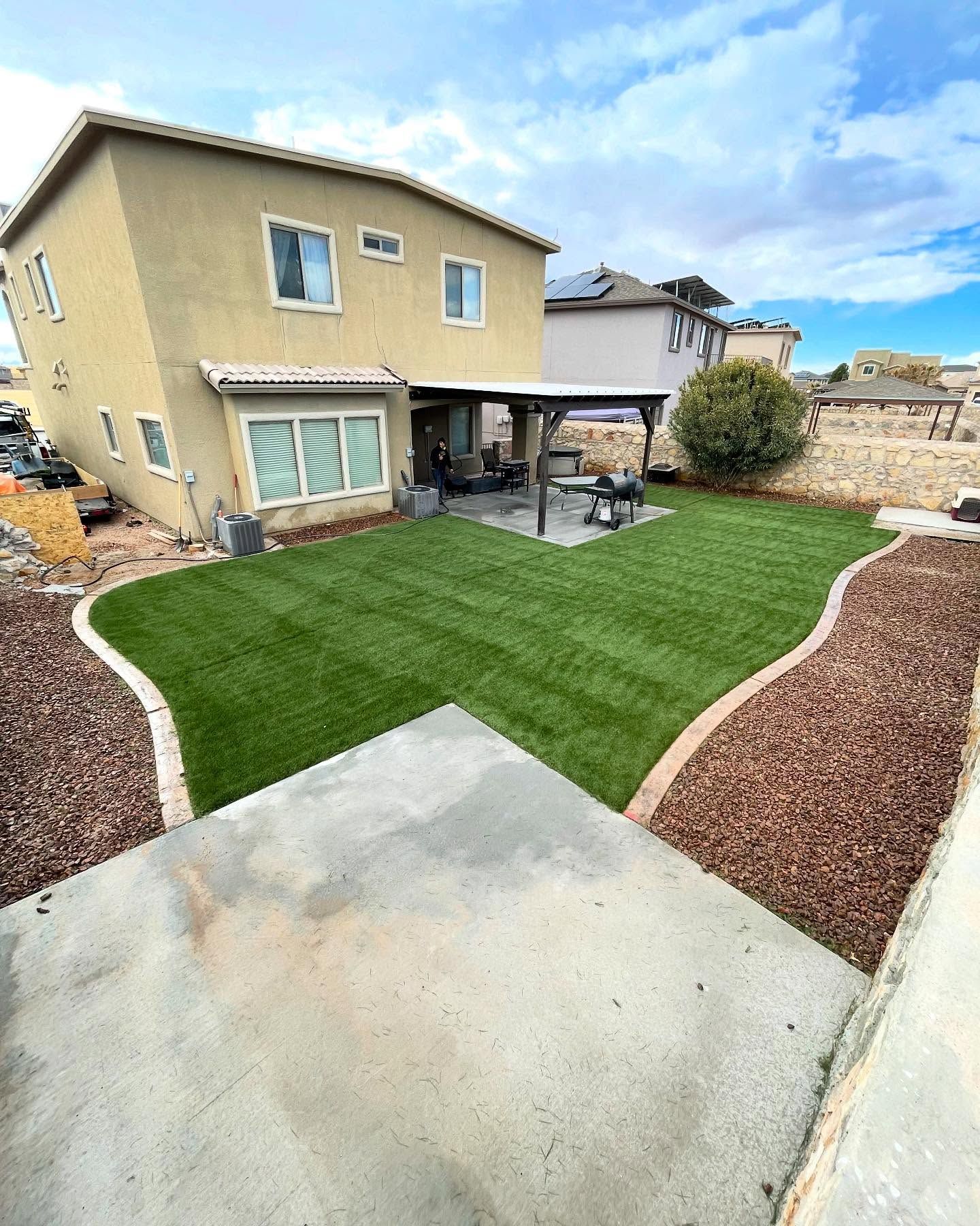 Backyard with fresh green lawn, concrete patio, and a two-story beige house under a partly cloudy sky