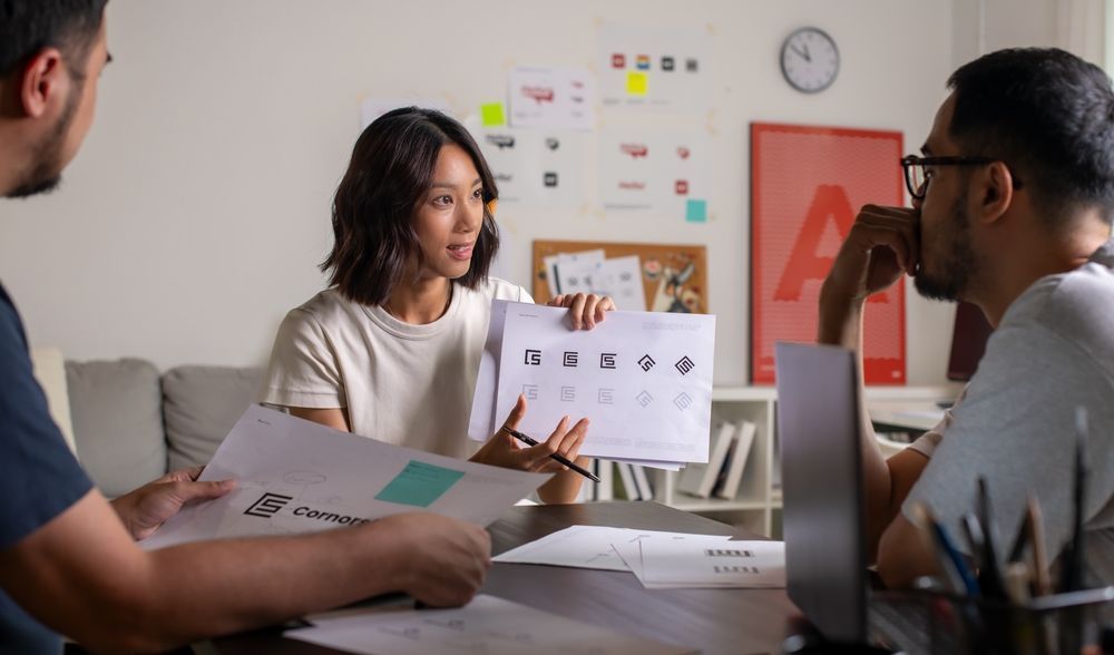 Woman presenting logo options to colleagues in a bright office setting.