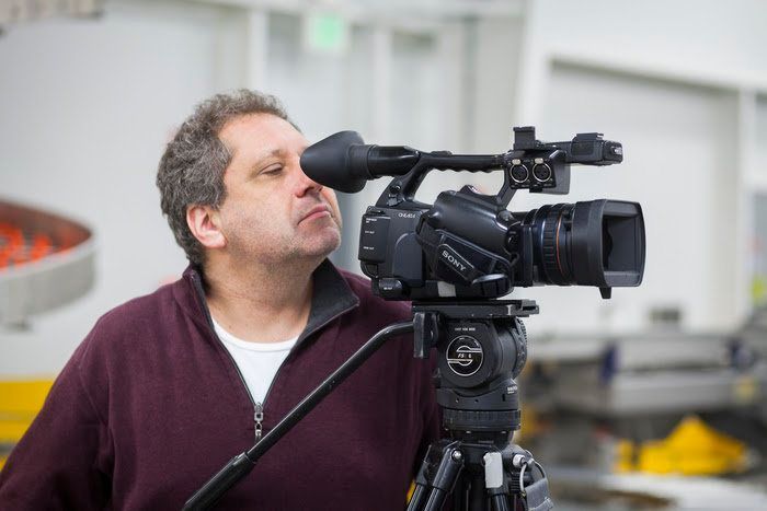 A man is standing in front of a video camera on a tripod.