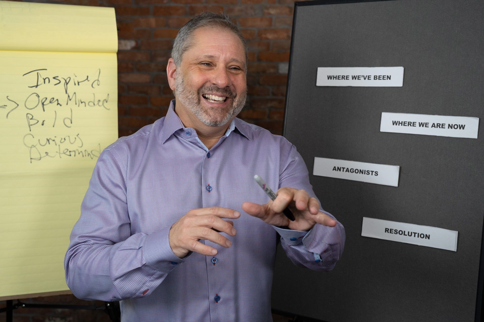 A man in a purple shirt is standing in front of a whiteboard with the words inspired written on it.