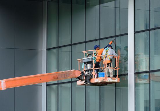 Two workers in a cherry picker cleaning an office window panel