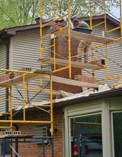 Worker on yellow scaffolding repairing a house roof and siding