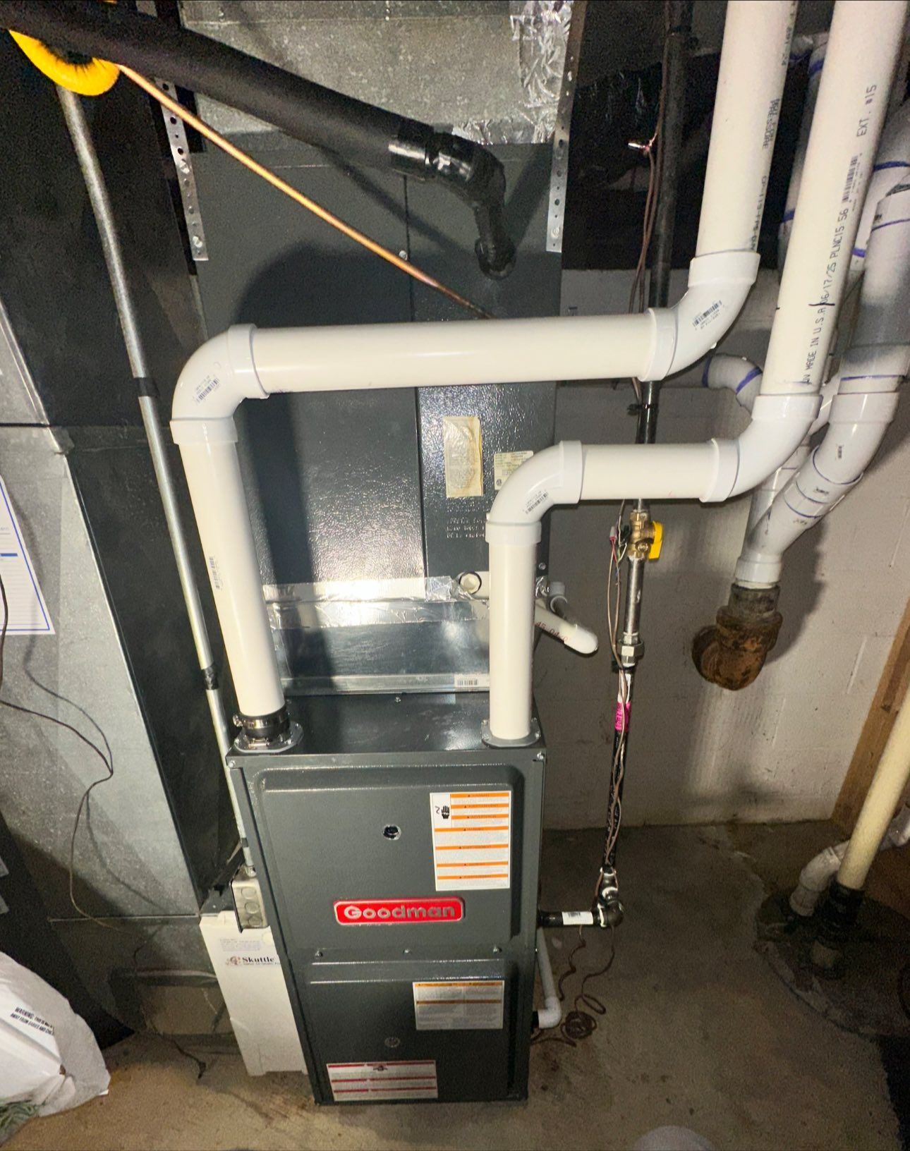 Basement furnace with white PVC pipes and utility lines against a concrete wall