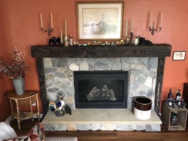 Fireplace with stone surround, wooden mantel, and decor, set against an orange wall.