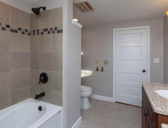 Bathroom with a bathtub, toilet, and vanity. Gray and tan tiles, light gray walls, white door.