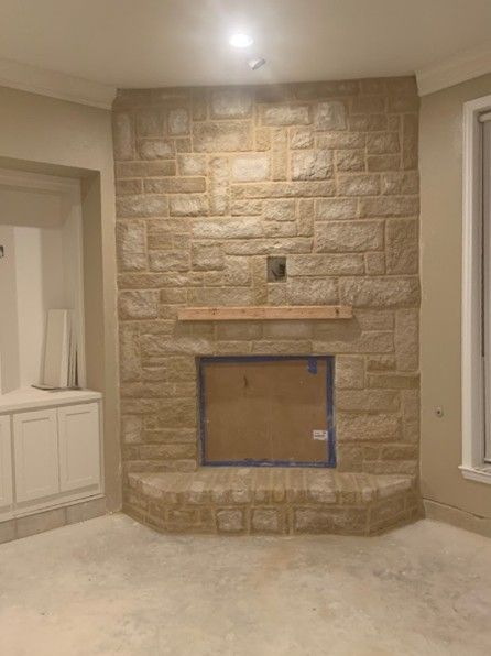 Stone fireplace in a room with light beige walls, wooden mantle, and a rectangular opening.