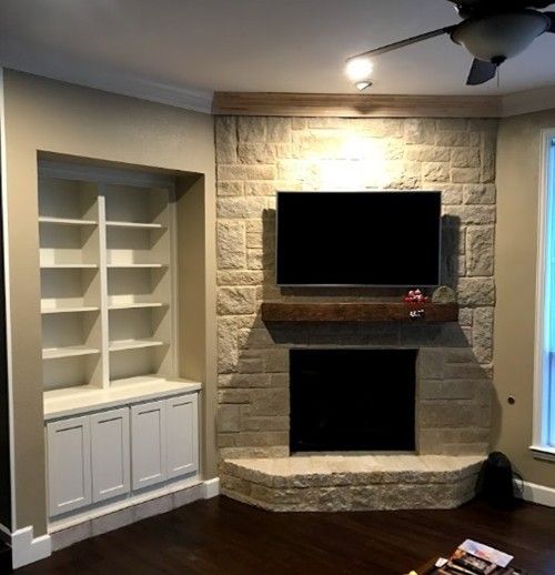Living room with stone fireplace, TV, built-in shelves, and dark wood floor.
