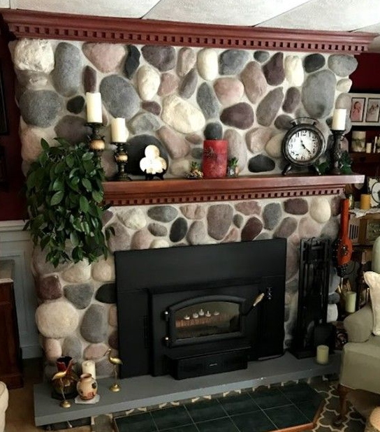 Stone fireplace with a dark insert, a wooden mantel, and decorative candles and plants.