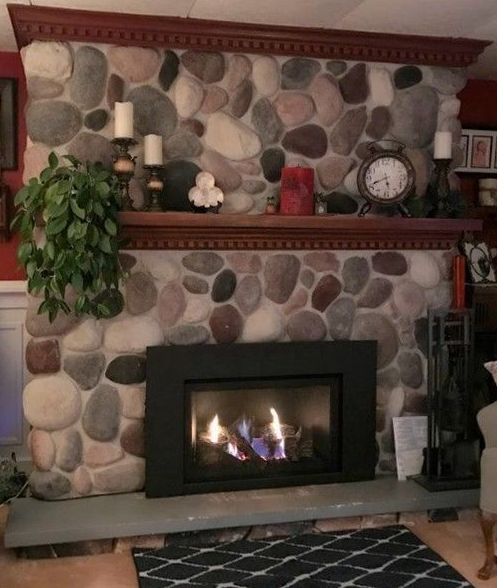 Stone fireplace with black framed fire, topped by a wooden mantel and decorative items.