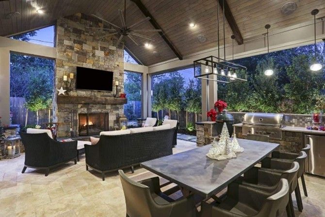 Covered outdoor living space with fireplace, dining area, and grill.
