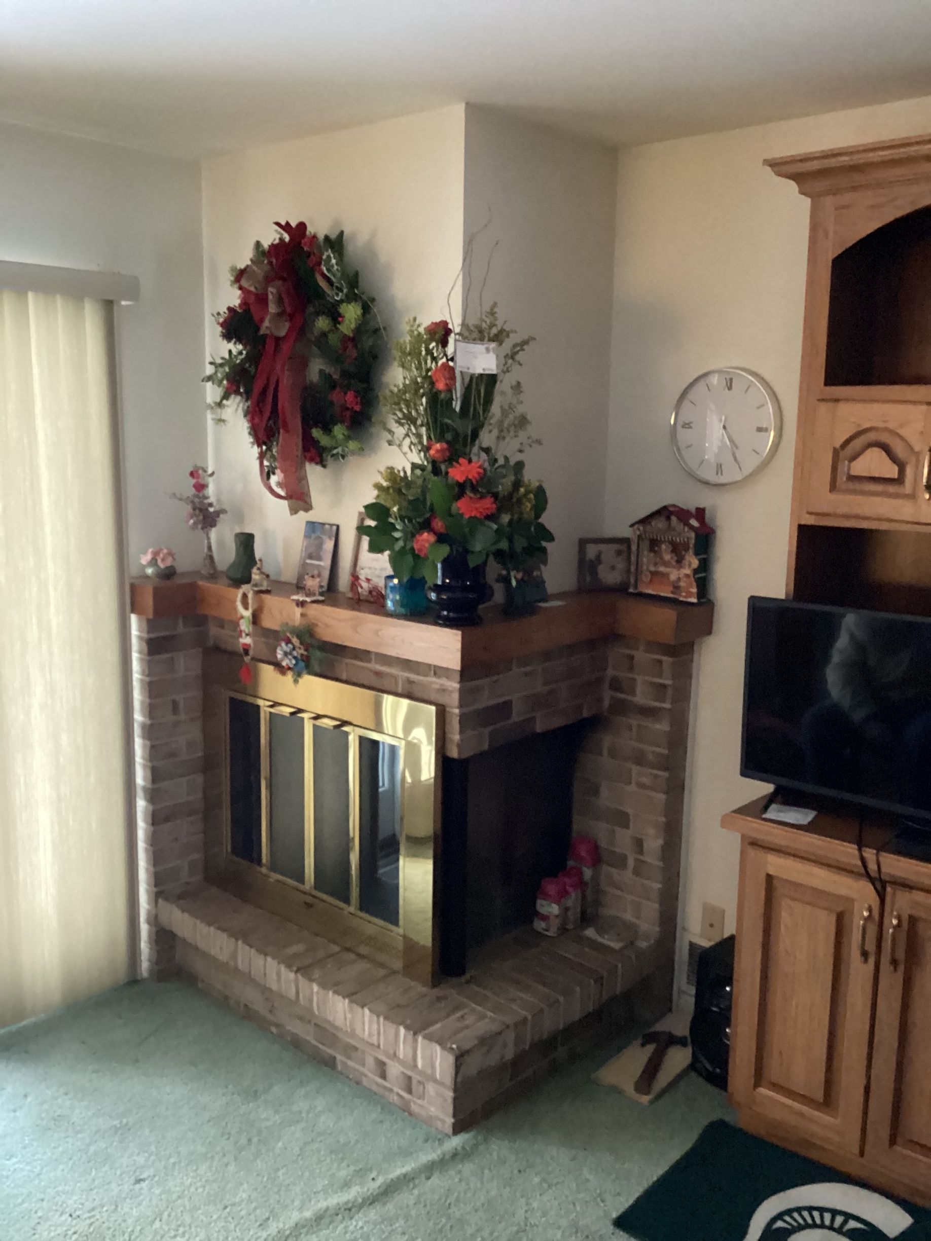 Living room fireplace decorated with wreaths and Christmas ornaments, beside a TV and wooden cabinet