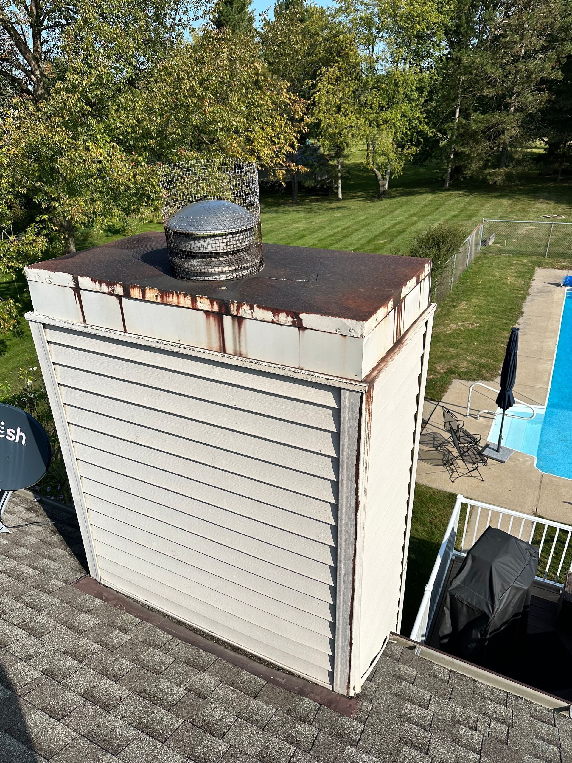 Rusted rooftop chimney vent on a white shingled utility structure beside a pool and yard