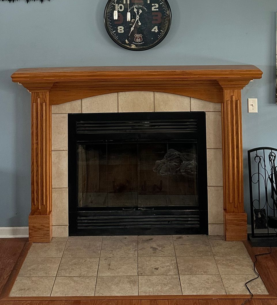 Stone fireplace with a black insert and wooden mantel, topped by a wall clock in a living room.