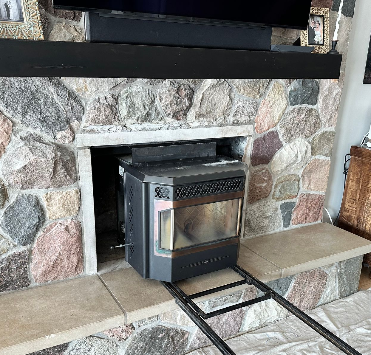 Wood-burning stove inserted into a stone fireplace with a black mantel and tiled hearth