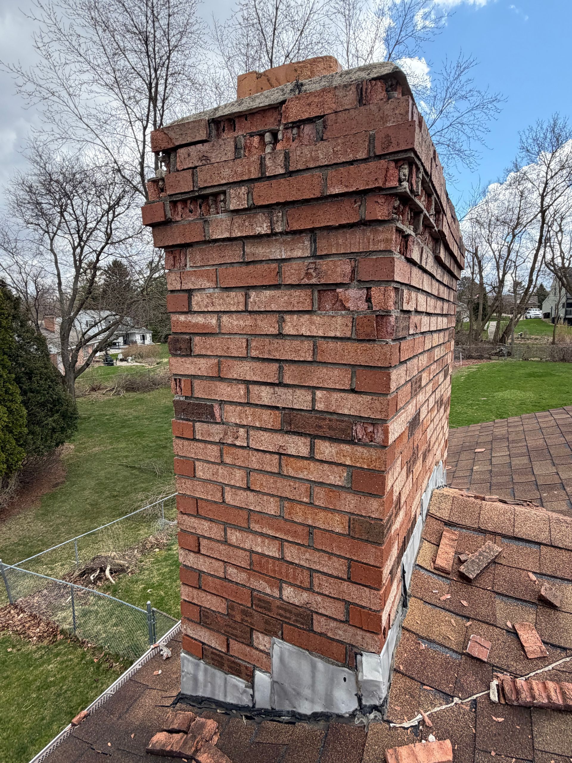 Damaged red brick chimney with a cracked top, standing outdoors in a grassy yard