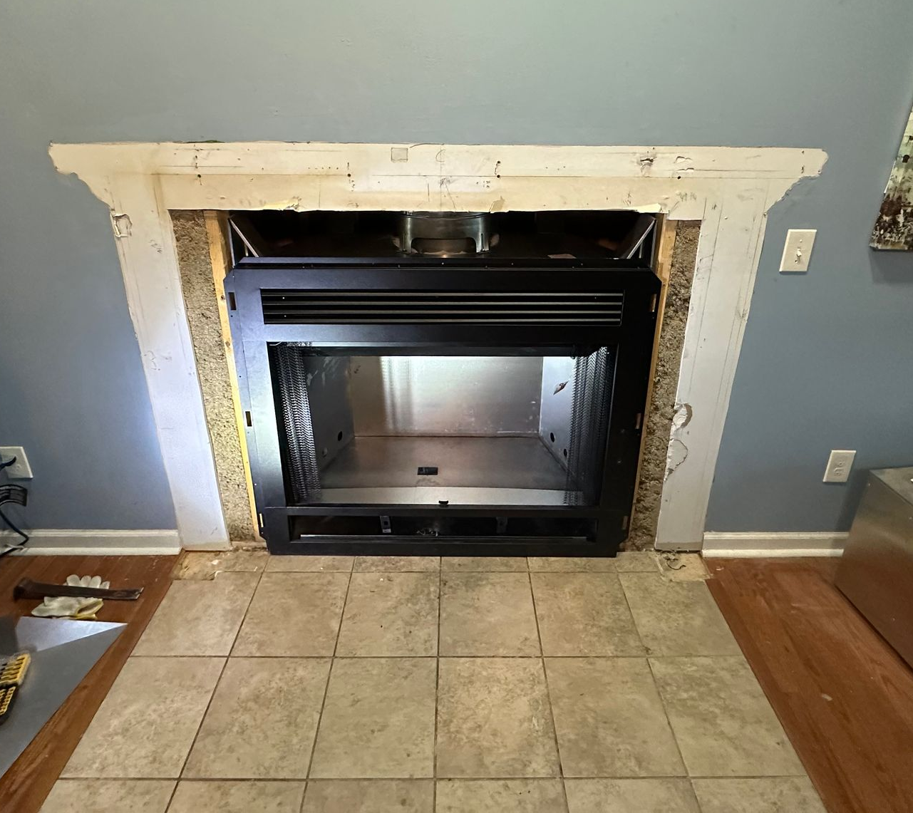 Black fireplace insert surrounded by white trim in a tiled hearth area with blue walls and hardwood floor edges