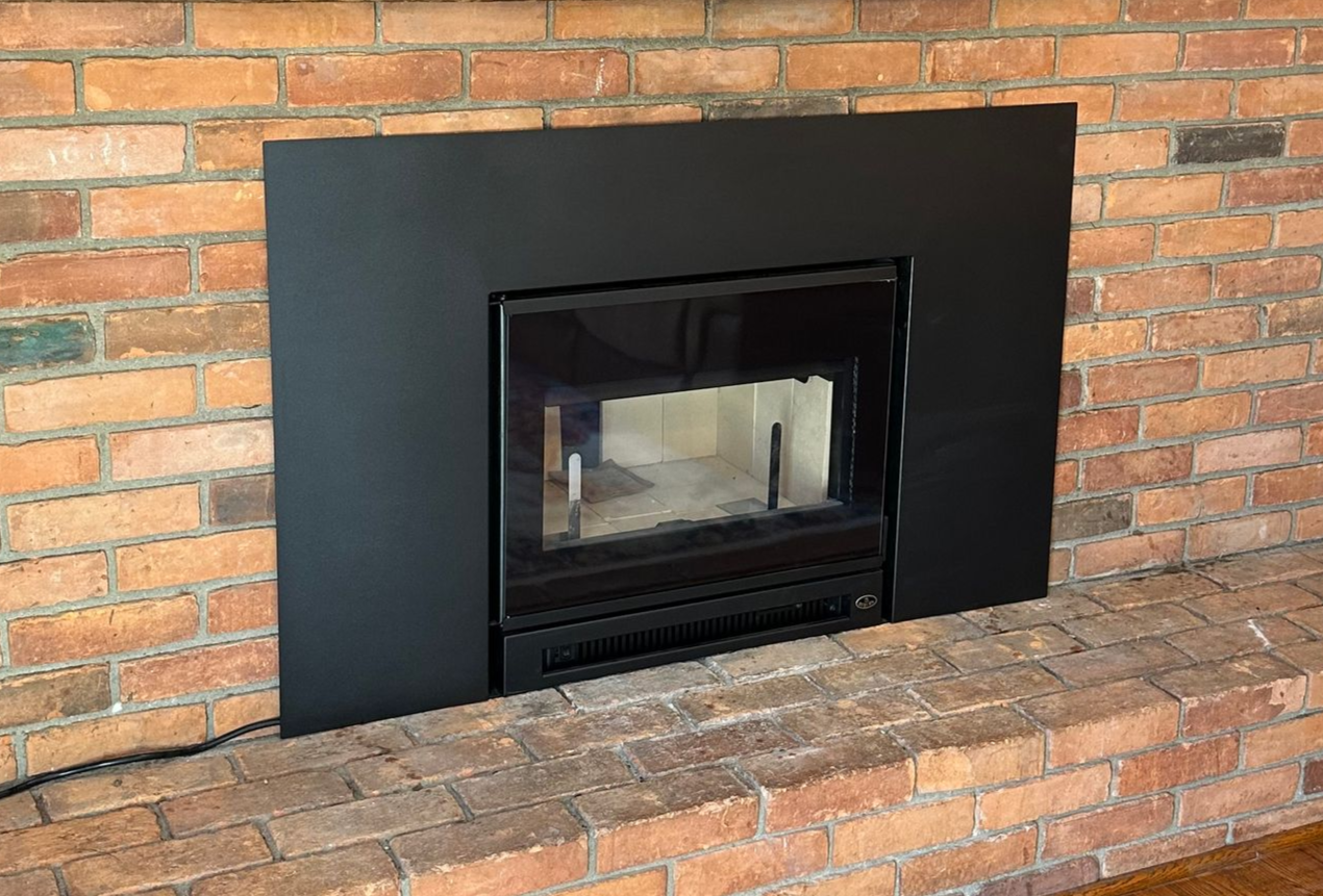 Black fireplace insert set into a red brick wall above a brick hearth.