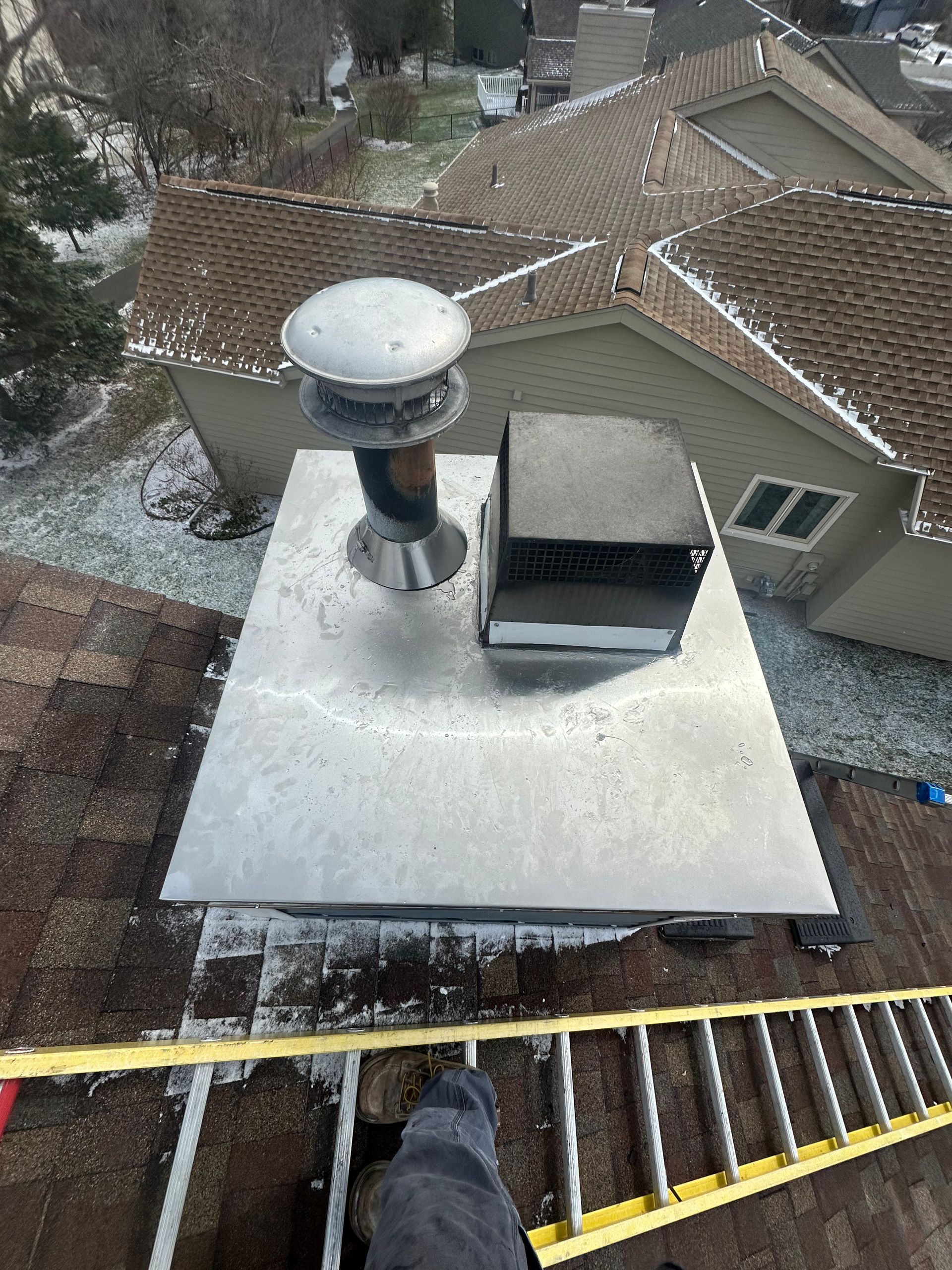 View from a rooftop ladder onto a flat white roof with a vent and snowy neighboring houses.