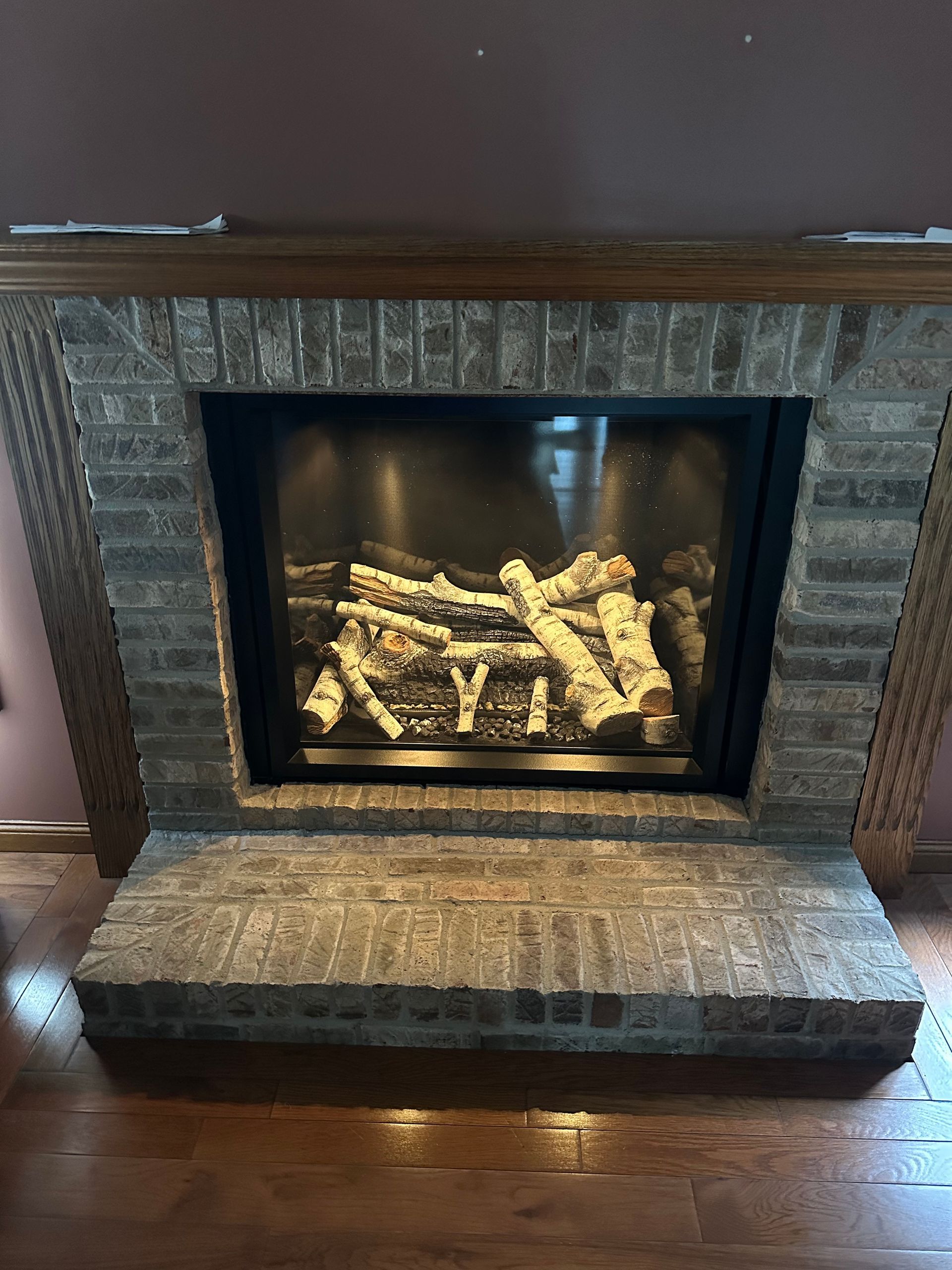 Stone fireplace with glass front and glowing logs above a matching hearth on a hardwood floor