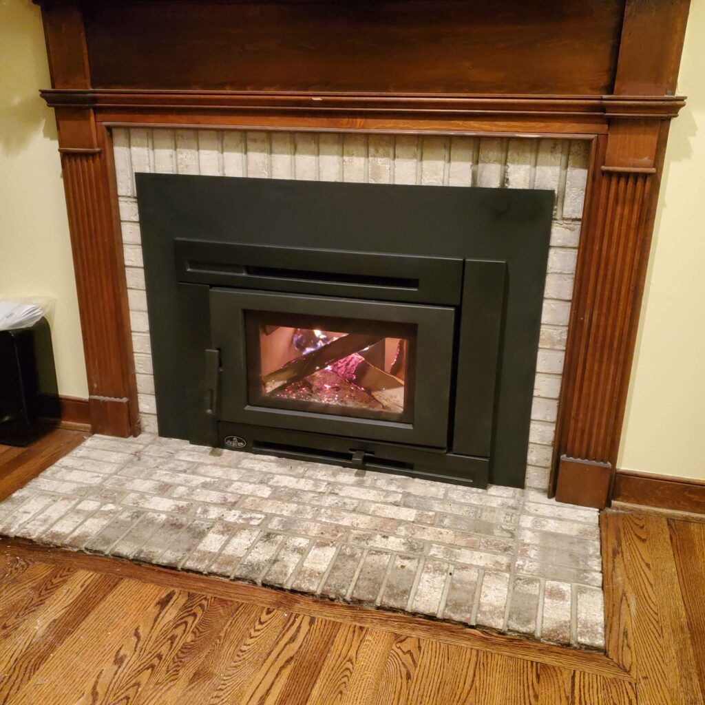 A lit gas fireplace with realistic logs, enclosed by glass and framed in patterned green and grey stone.