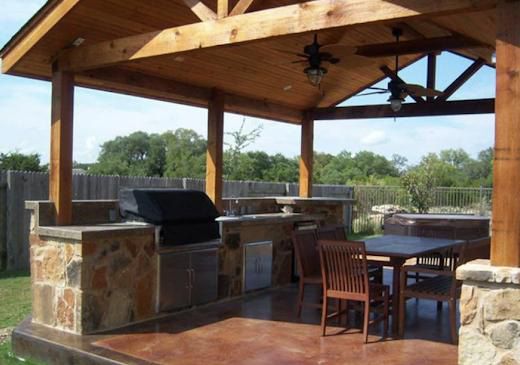 Outdoor kitchen with a wooden pergola, built-in grill, stone accents, table and chairs.