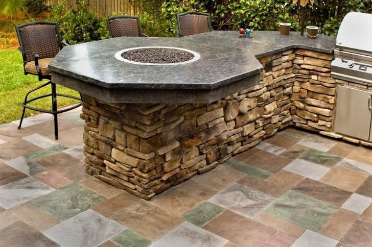 Outdoor kitchen island with fire pit, stone base, and granite countertop; chairs are at the bar.