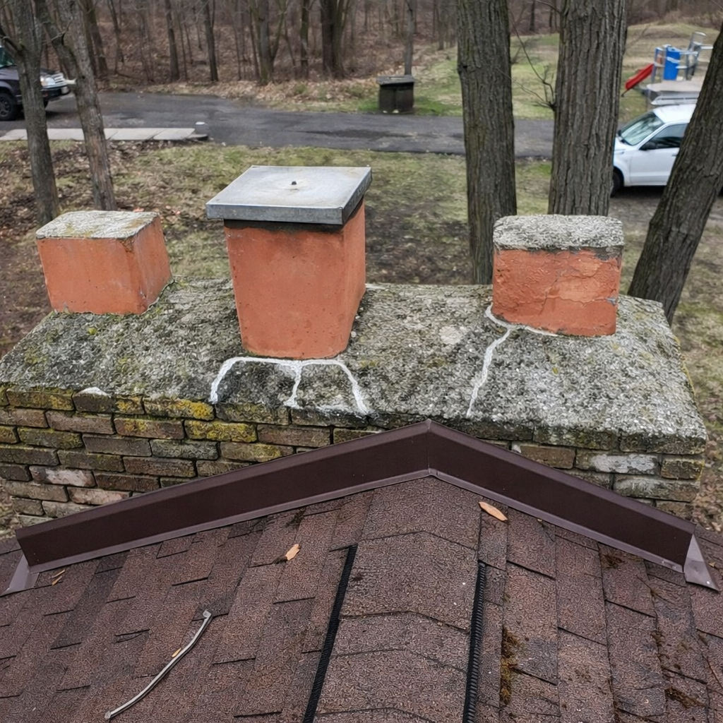 Brick rooftop below three orange chimney stacks on a mossy stone wall in a wooded yard