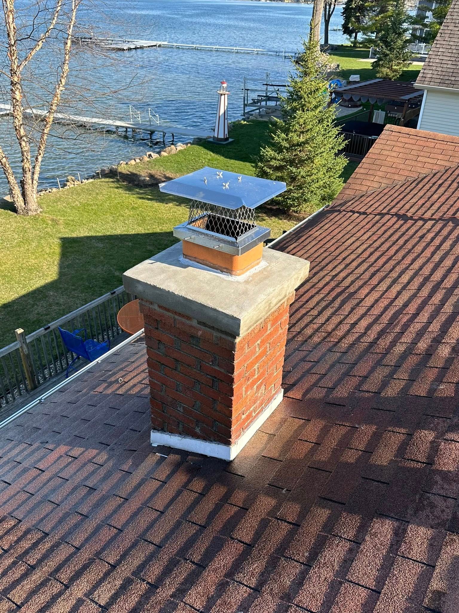 Rooftop chimney beside a red shingle roof, overlooking a lake and grassy shoreline.