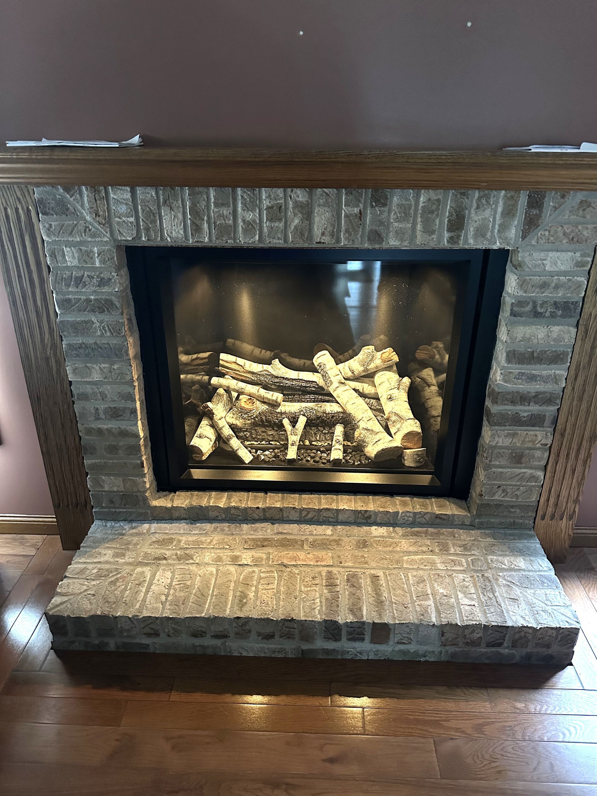 Lit electric fireplace with stone surround and matching hearth in a room with hardwood floors