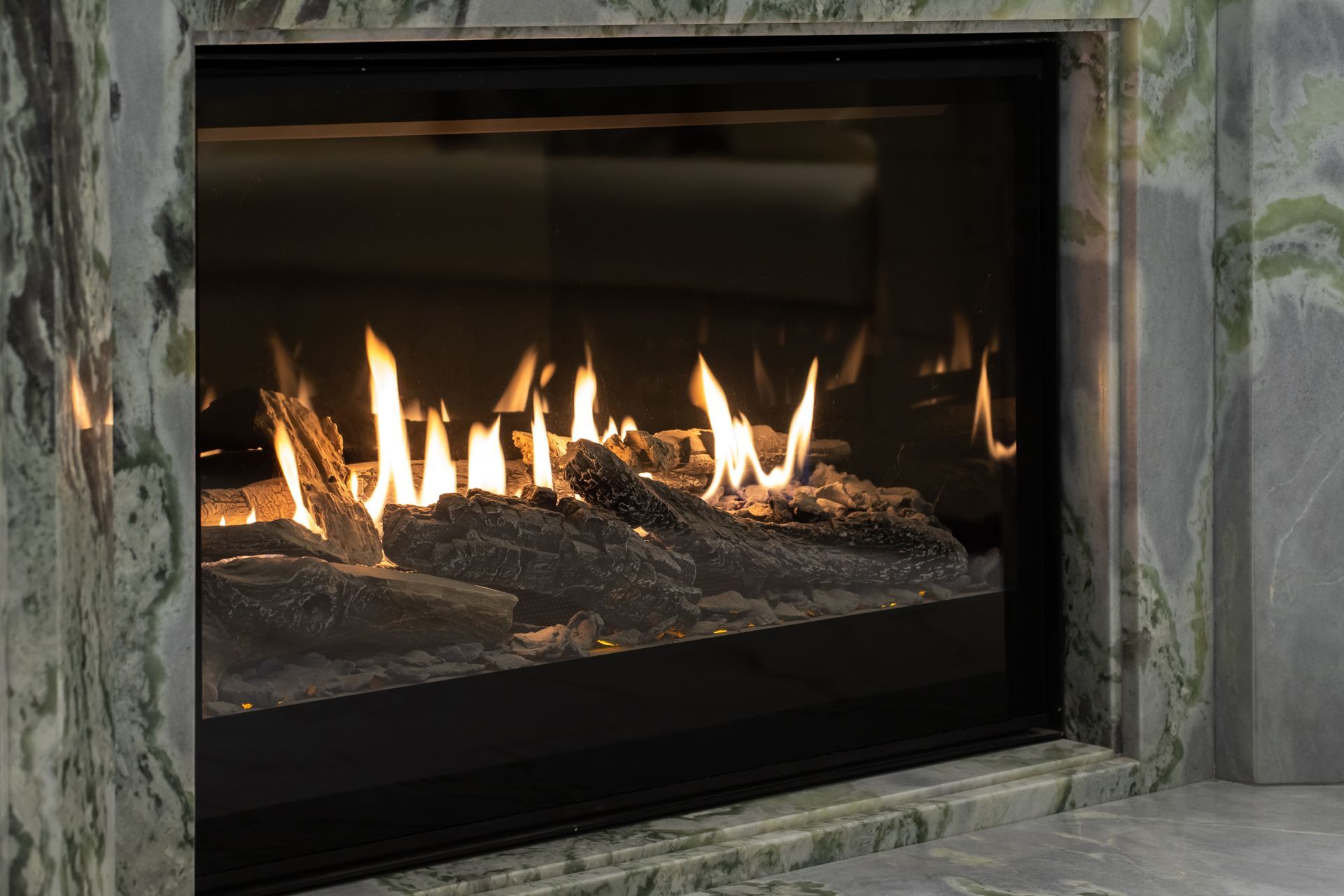 A gas fireplace with glowing flames, artificial logs, and a green marble surround.