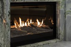 Modern fireplace with bright flames behind glass, set in a gray stone surround