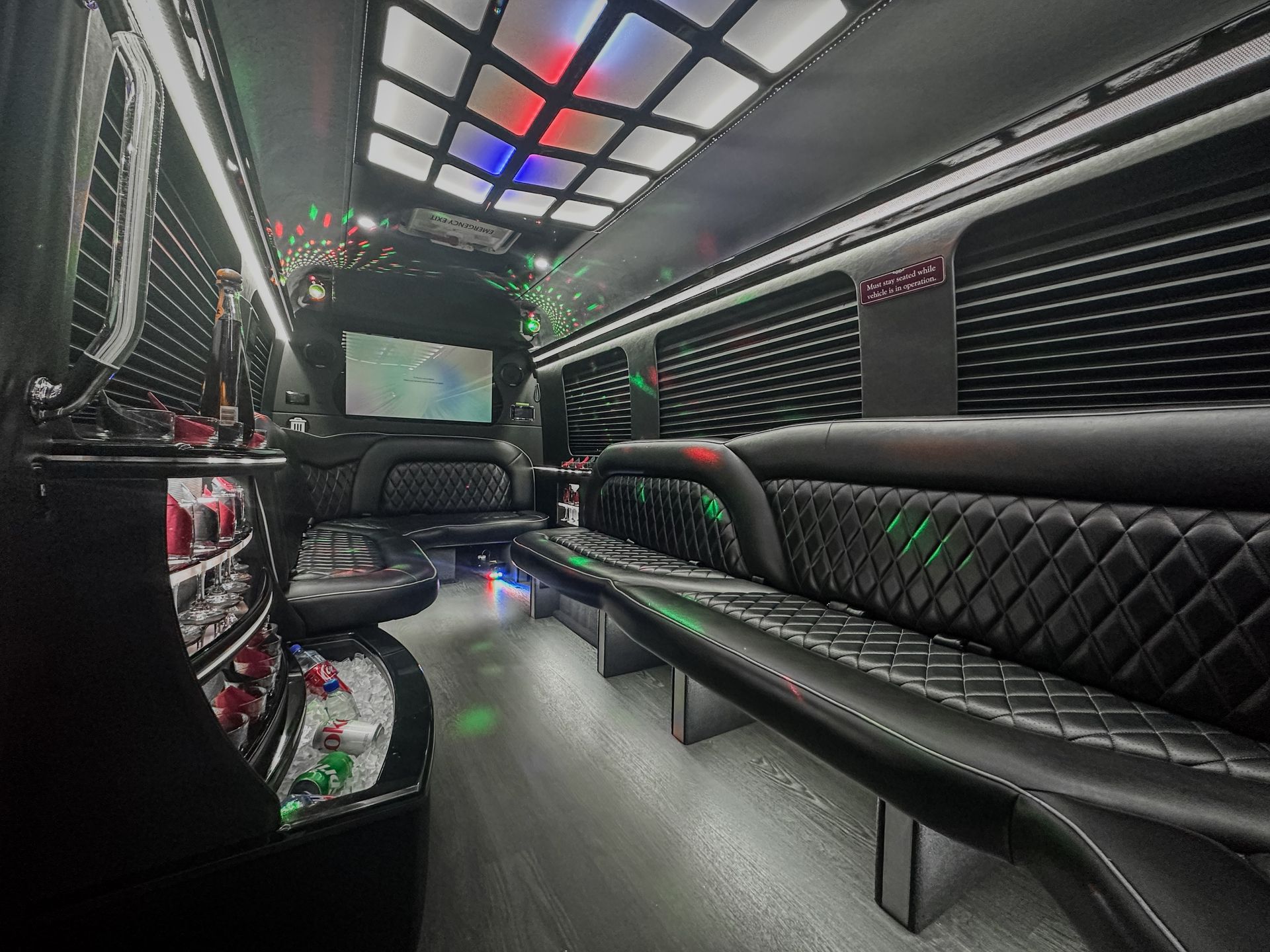 Luxury Sprinter limousine interior with quilted leather wraparound seating, ambient ceiling lighting, entertainment screen.