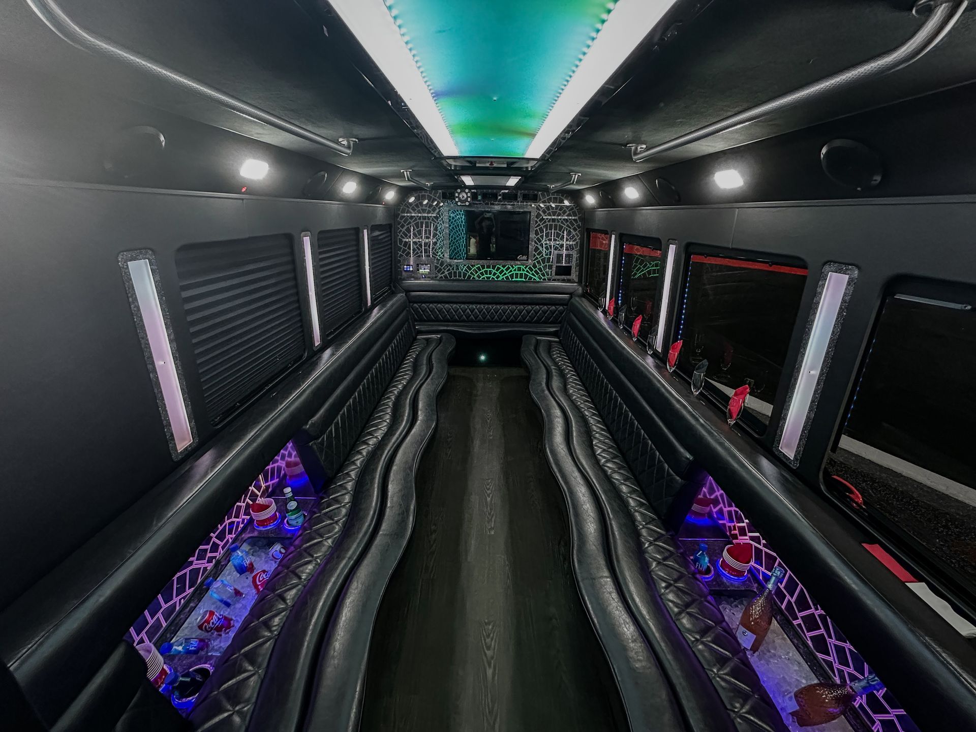 Luxury limo-style party bus interior with wraparound leather seating, LED mood lighting, beverage coolers.