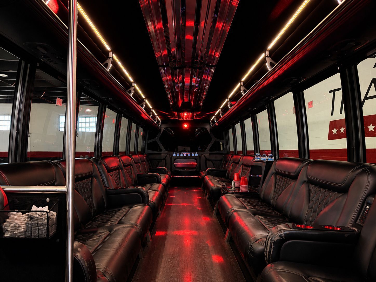 Spacious party bus interior with black leather seats, red accent lighting, and entertainment features