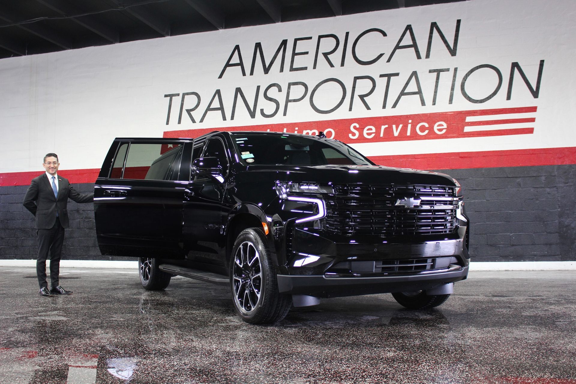 Chauffeur holding the door open beside a black Chevrolet Suburban at American Transportation