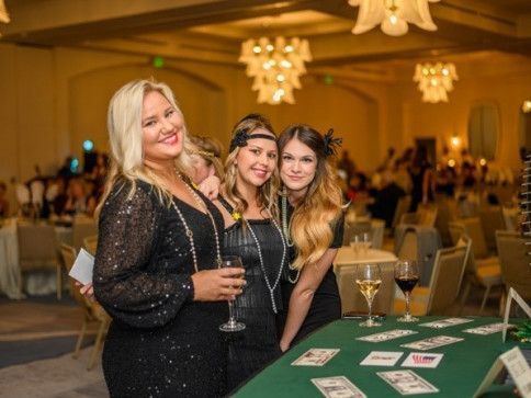 Three women are posing for a picture in front of a table with cards and wine glasses.