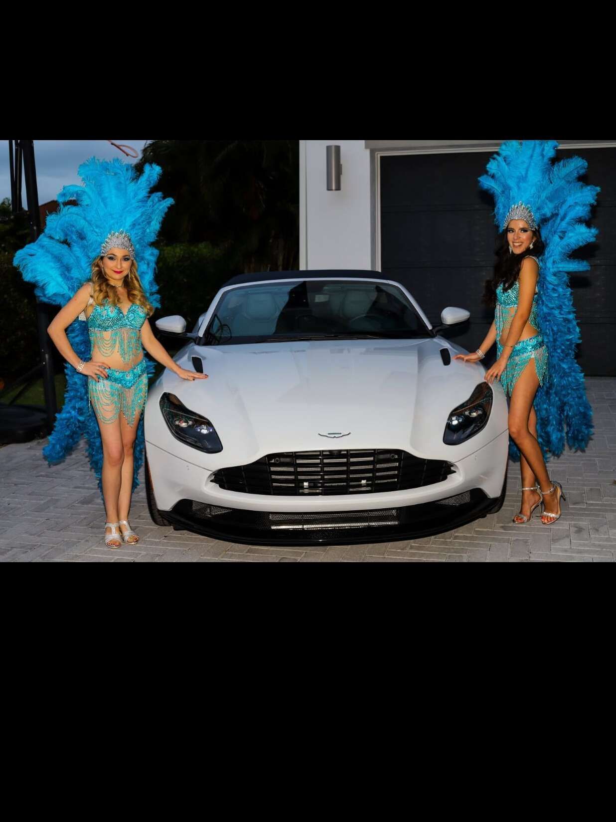 Showgirls posing in front of a Aston Martin car for a James Bond theme party.