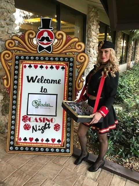 Cigarette girl posing in front of a welcome marquee sign at a Speakeasy party.