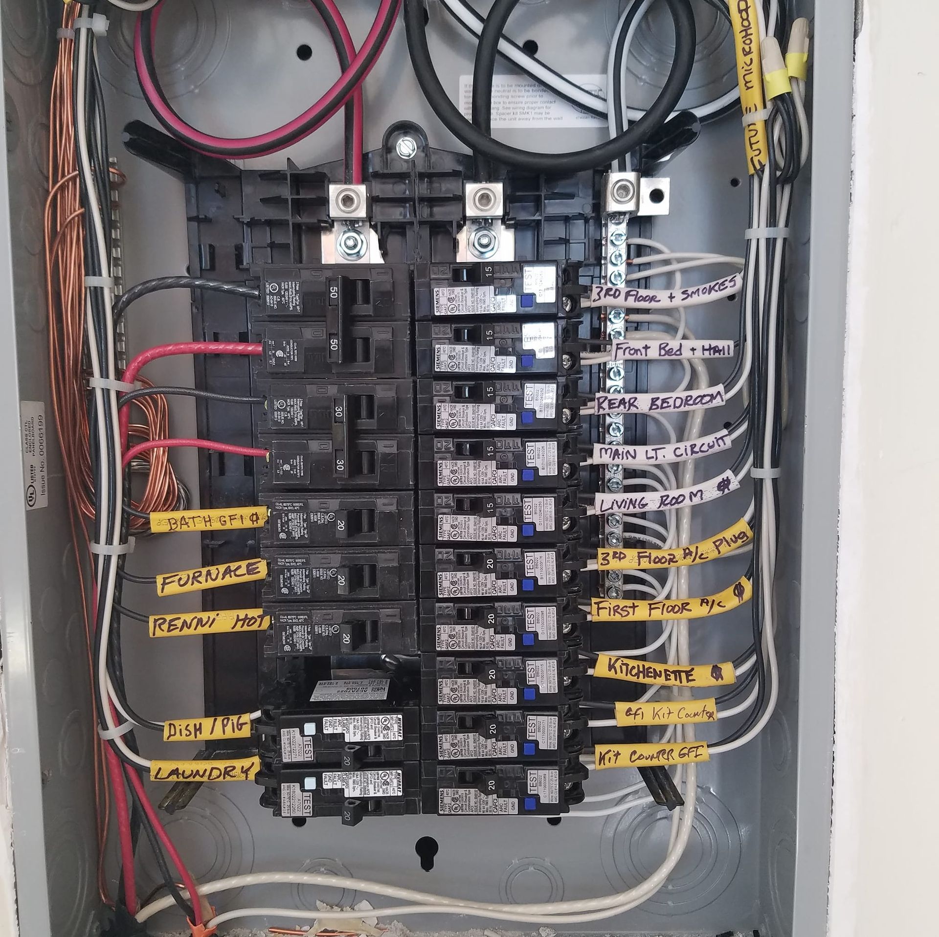 Open electrical breaker panel with labeled circuits and bundled wires.