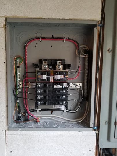 Open electrical breaker panel with red and white wiring inside a wall cabinet