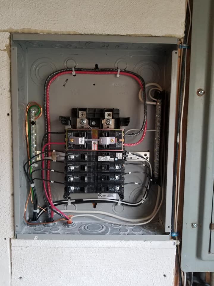 Open electrical breaker panel with red and white wiring inside a wall cabinet.