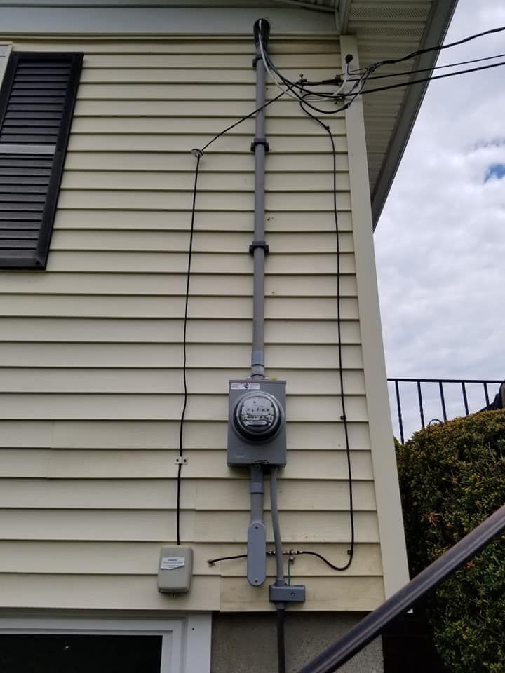 Electrical meter and conduit mounted on a beige house exterior with overhead wires.