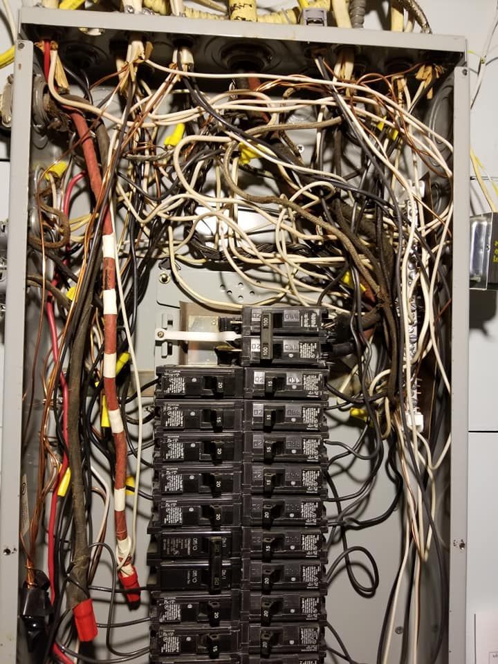 Open electrical panel with tangled wires and stacked circuit breakers.
