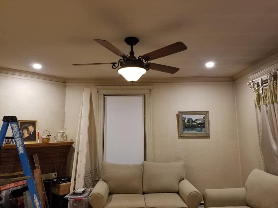 Living room with beige sofa, ceiling fan, fireplace, ladder, and framed wall art