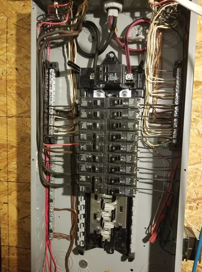 Open electrical breaker panel with exposed wires and circuit breakers inside a wall cavity