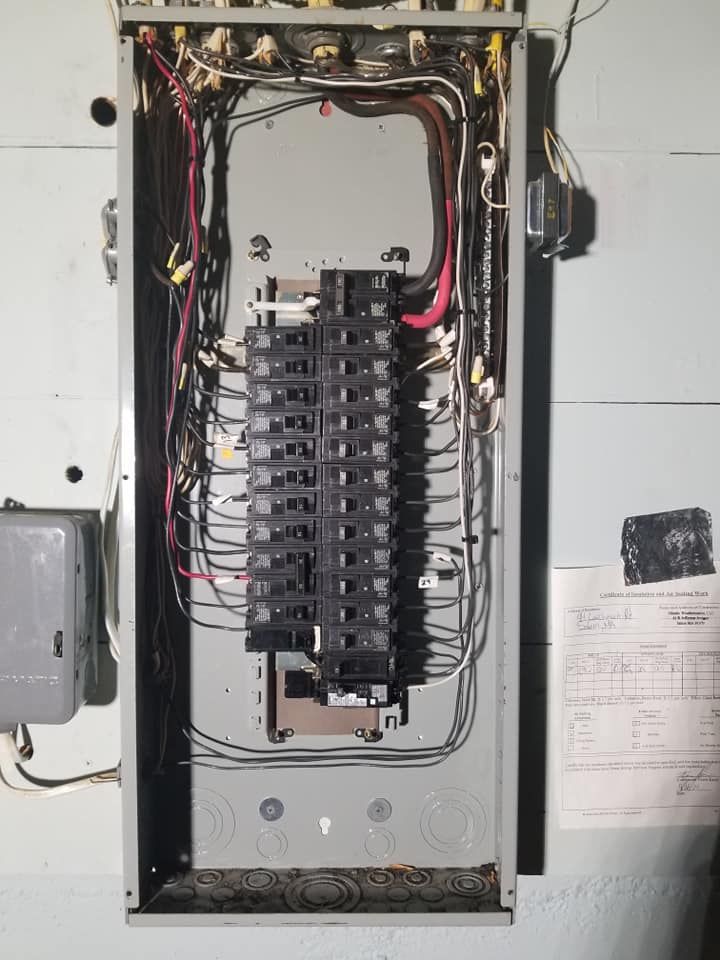 Open electrical breaker panel with exposed wiring and multiple circuit breakers in a wall-mounted box