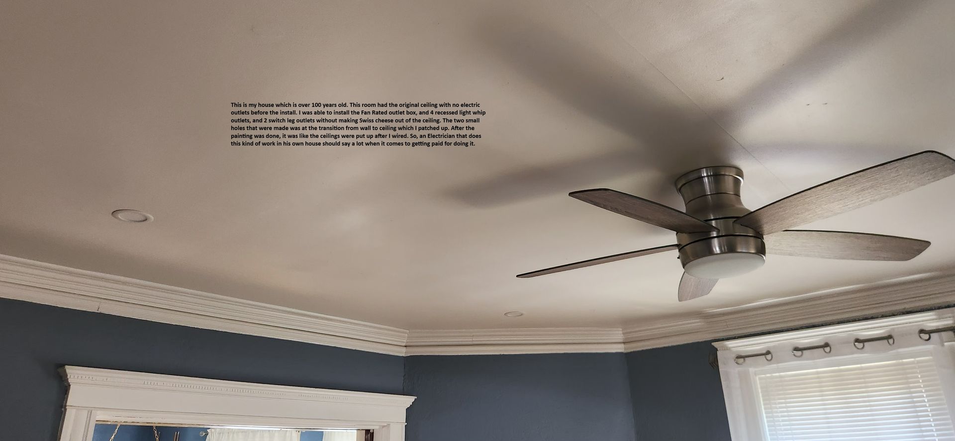 Ceiling corner with a fan, crown molding, blue walls, and a window with white curtains.