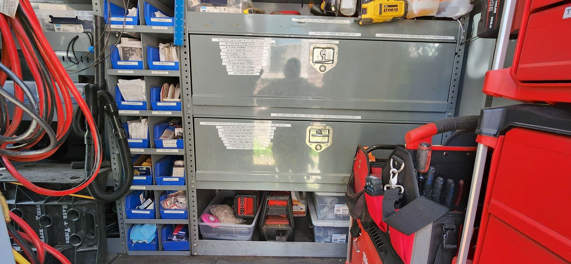 Cluttered workshop with stacked gray tool chests, red tool cabinets, and coiled cables